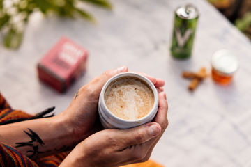 Hands holding a guaraná latte with a product box and softly blurred canned energy drink in the background